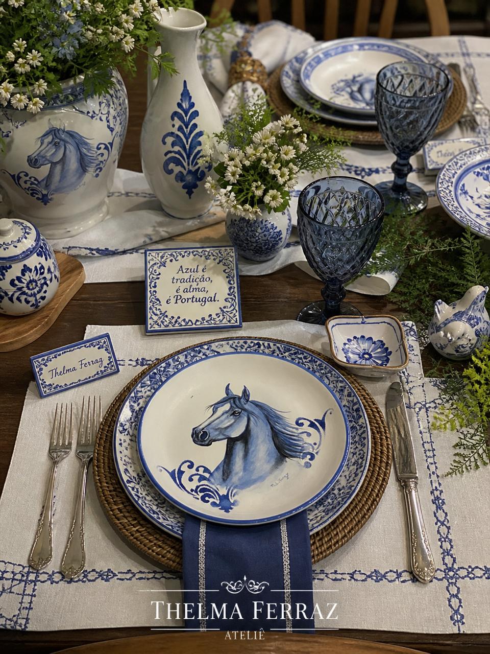 Mesa posta com pratos, vaso e jarra de cerâmica em azul e branco com cavalos pintados à mão