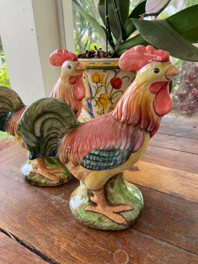 Dois galos de cerâmica pintados à mão sobre uma mesa de madeira