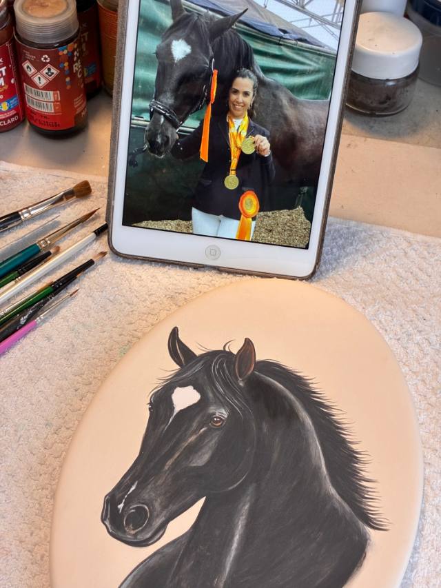 Placa oval com retrato de cavalo preto pintado à mão, ao lado do tablet com a foto de referência
