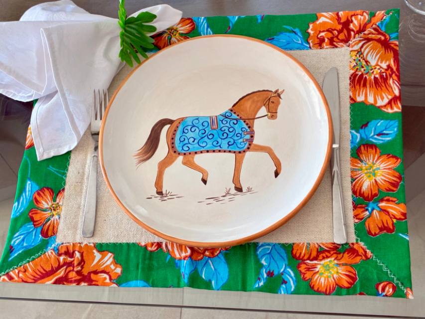 Prato de cerâmica com cavalo de capa azul sobre toalha de chita florida