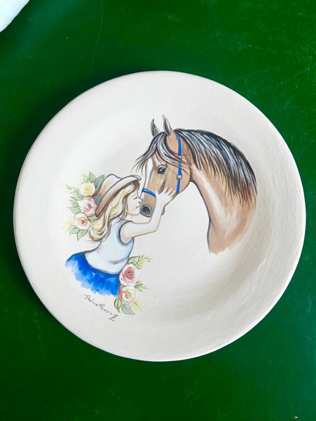 Prato de cerâmica com menina de chapéu beijando o focinho de um cavalo, com flores