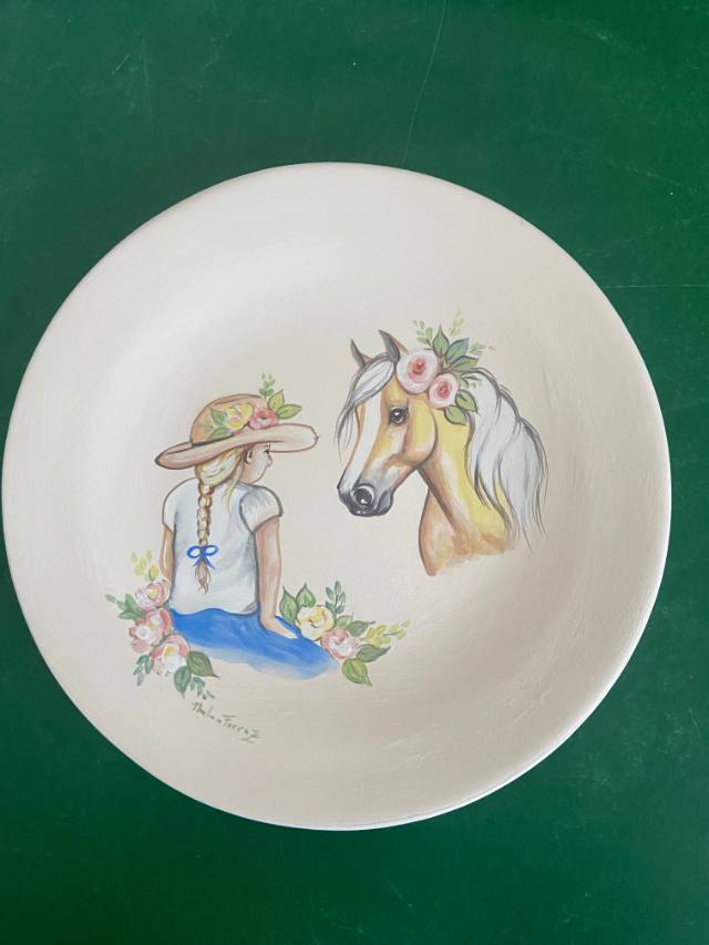 Prato de cerâmica com menina de trança e chapéu ao lado de um cavalo palomino com flores na crina