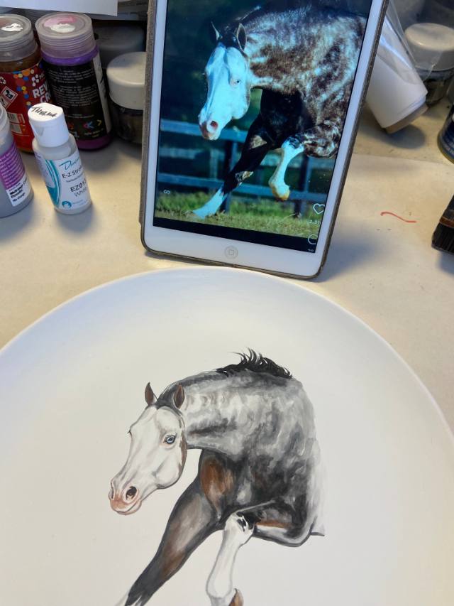 Prato de cerâmica com retrato de cavalo tordilho em andamento, ao lado do tablet com a foto de referência