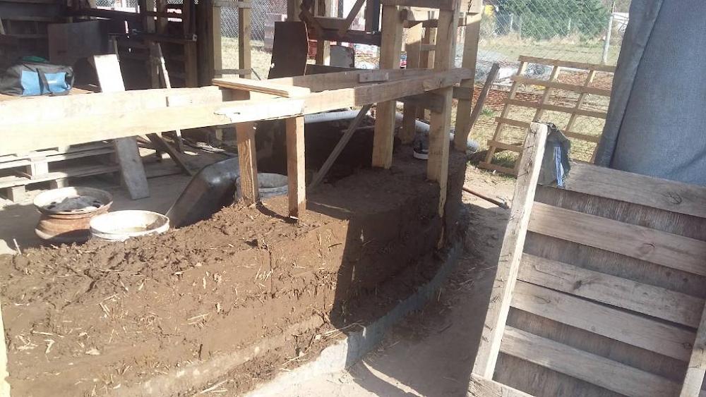 Muro curvo de barro y paja en pleno proceso de bioconstrucci&oacute;n con estructuras de madera en el terreno de Alma de Hornero.