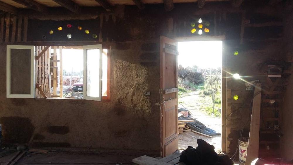 Interior de la casa de barro de Alma de Hornero mostrando la luz natural filtr&aacute;ndose a trav&eacute;s de botellas de vidrio incrustadas en las paredes.