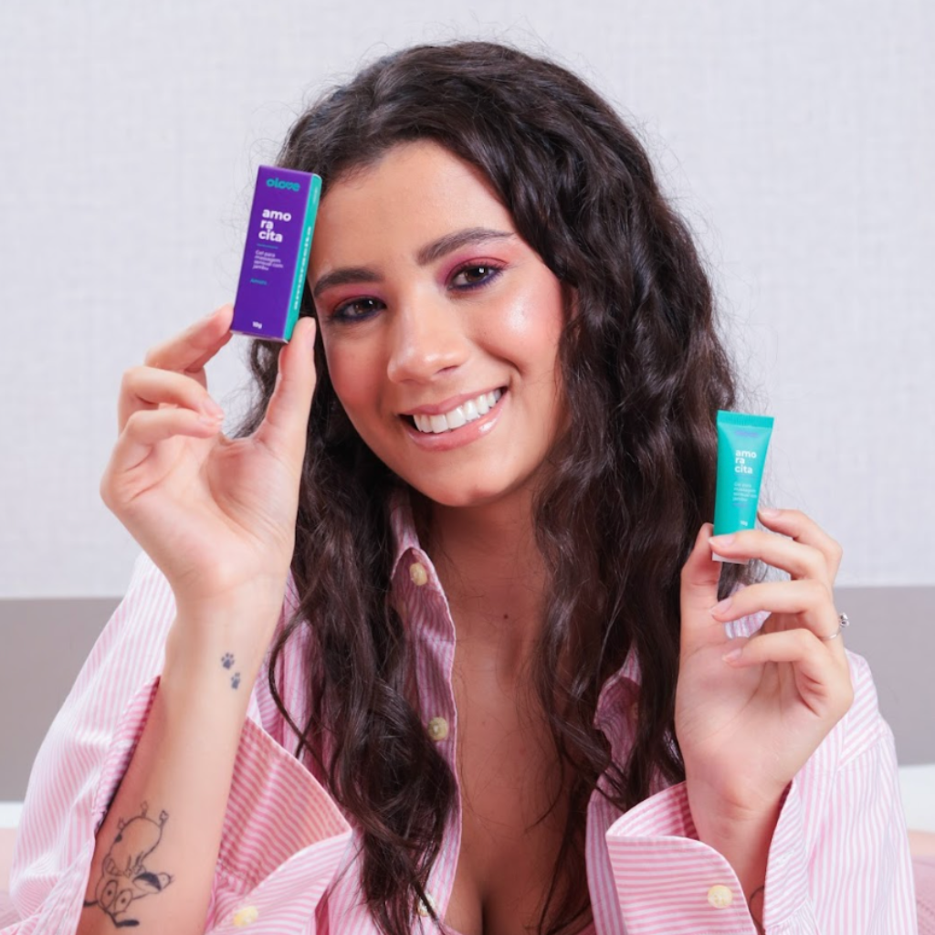Mulher sorridente segurando embalagem roxa e tubo verde do Gel Excitante Jambu Amoracita