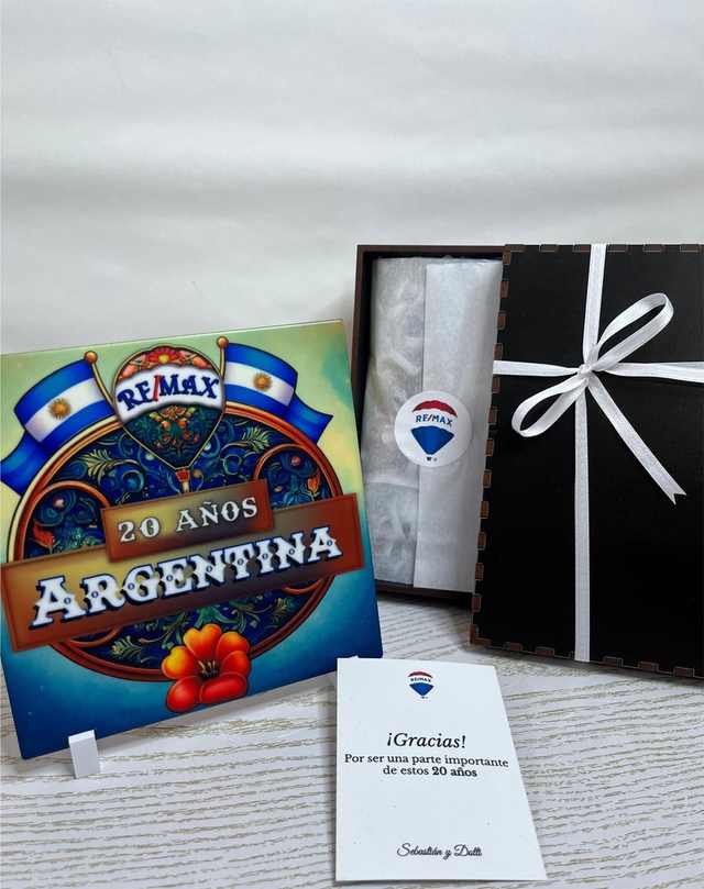 Azulejo RE/MAX junto a su caja de madera abierta y la tarjeta de agradecimiento