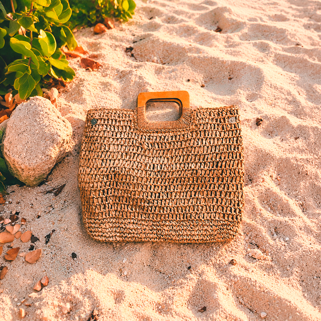 Cartera de rafia calada color caramelo con asas de madera sobre la arena
