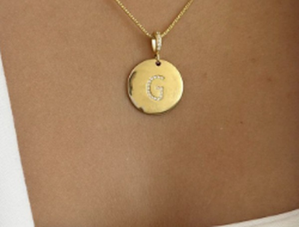Close da medalha gravada com a letra G e zirc&ocirc;nias