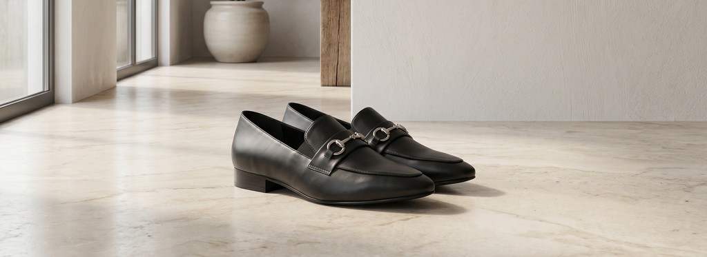 Mocasín Amelie negro sobre piso de mármol en interior minimalista, contexto editorial