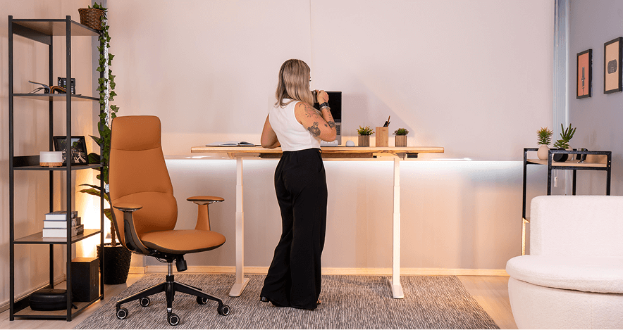 Mesa com regulagem de altura F50 em altura para uso em pé, ambientada ao lado de modelo feminina. Visão fotográfica frontal