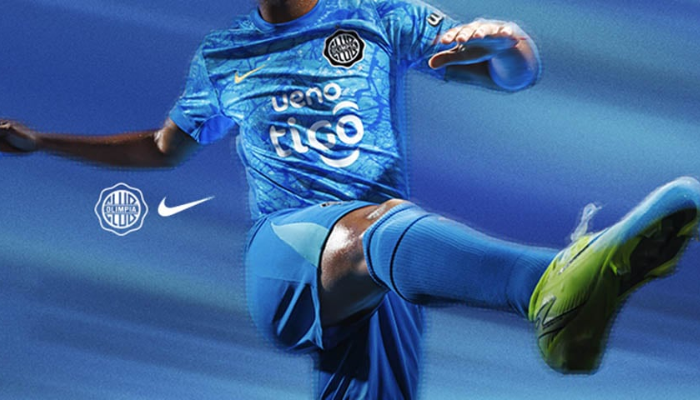 Camisa terceira do Club Olimpia Nike 2025 azul celeste com detalhes dourados, selo interno com bandeira do Uruguai e textura marmorizada no tecido.
