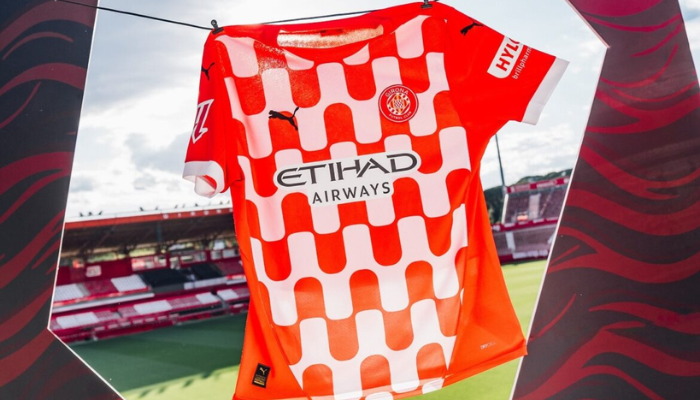 Camisa titular do Girona FC 2024-2025: design "vaire" inspirado nos escudos do clube e da cidade. Vermelho vibrante, branco elegante, gola redonda, punhos brancos e bandeira da Catalunha na nuca. Logo Puma para um toque moderno.