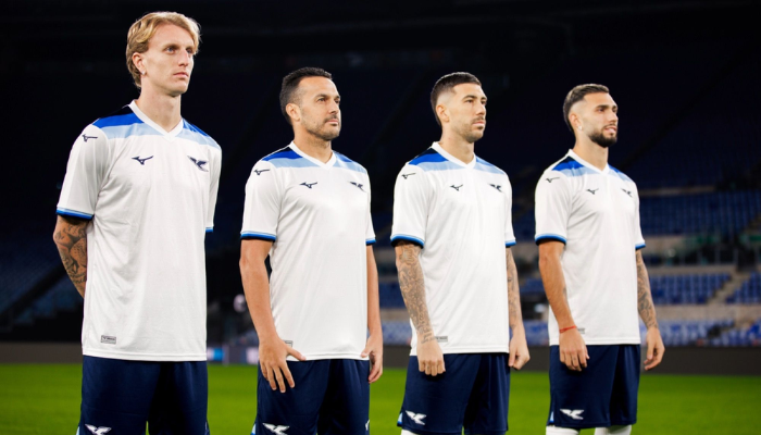 Camisa Lazio 125 Anos Mizuno 2025, modelo comemorativo branco com jacquard em chevrons. Gola V branca, faixas retr&ocirc; nos ombros e punhos em tr&ecirc;s tons de azul. Escudo cl&aacute;ssico com &aacute;guia em azul marinho, logo da Mizuno na mesma tonalidade. Inscri&ccedil;&atilde;o "9 gennaio 1900" na nuca, celebrando a funda&ccedil;&atilde;o da Lazio.