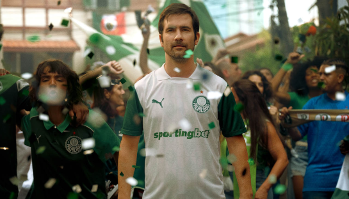 Camisa Reserva do Palmeiras 2025 da Puma, predominantemente branca com estampa em jacquard. As mangas são verdes e a gola polo branca traz a frase “De fato é campeão” no interior.