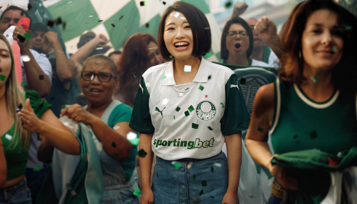 Camisa Palmeiras II 2025 Feminina, cor branca com mangas verdes, gola polo branca, estampa jacquard exclusiva, escudo oficial do Palmeiras no lado esquerdo do peito, logo PUMA em verde no lado direito e em branco nas mangas, além do patrocínio Sportingbet aplicado em verde. Frase “De Fato é Campeão” na parte interior da gola.