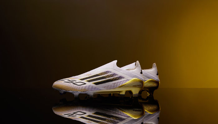 Chuteira Adidas F50 Elite FG Laceless nas cores branca, dourada, preta e roxa com design moderno, sem cadarço, ideal para velocidade e controle em campo.