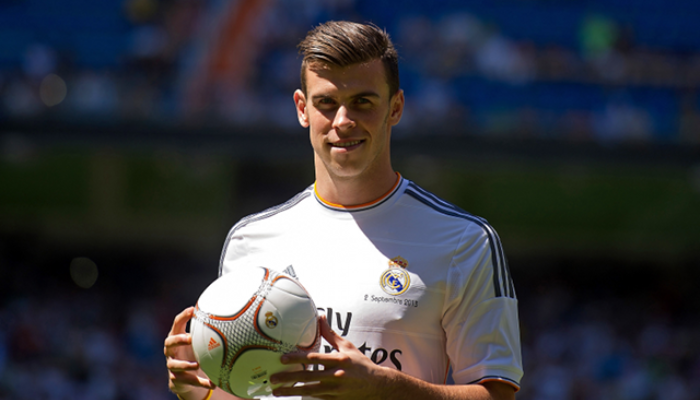 camisa home retro do Real Madrid da temporada 2013-14. A camisa é predominantemente branca com listras pretas finas e detalhes em laranja na gola V, nas mangas e na barra inferior. O escudo do Real Madrid está bordado no lado esquerdo do peito e o logotipo da Adidas está nas mangas.