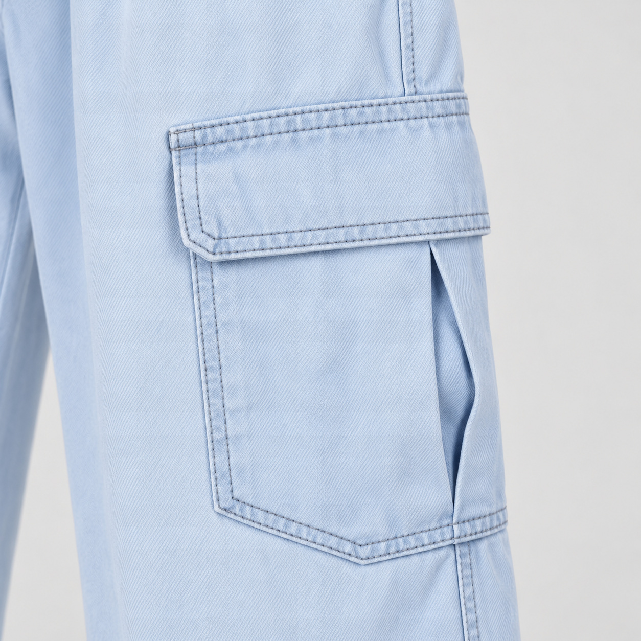 Bolso cargo com aba, costuras aparentes e textura do jeans azul-claro.