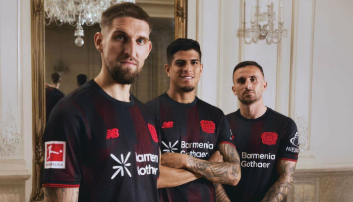 Camisa Titular Bayer Leverkusen 2025-26 New Balance preta com linhas vermelhas, escudo e logo em vermelho, padrão cruzado, inscrição Werkself na nuca.