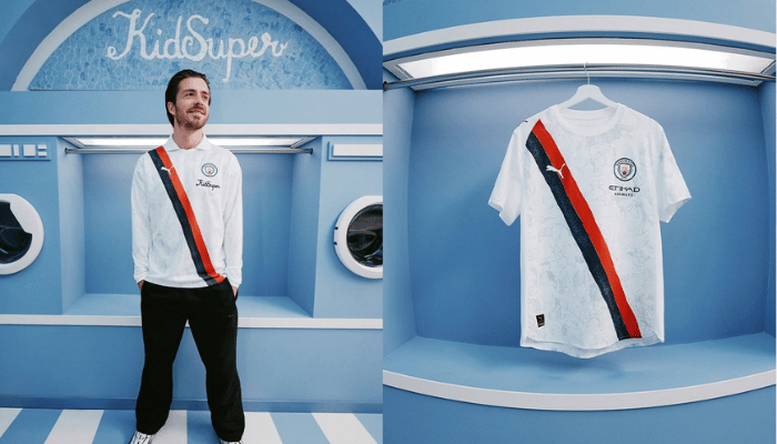 Camisa Manchester City 2025 titular branca, com faixa diagonal preta e vermelha, grafismo Poznan no corpo, gola branca, escudo City e logos PUMA e KidSuper em destaque