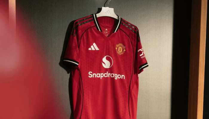 Camisa titular Manchester United 2025 2026 Adidas, vermelha com grafismos nos ombros, gola V com nuca preta, listras pretas nas laterais e escrita “Theatre of Dreams” nas costas