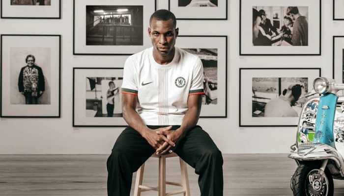 Camisa reserva Chelsea 2025 2026 Nike, branca com faixa vertical preta e laranja, gola redonda branca, escudo no peito esquerdo e Swoosh preto no lado direito