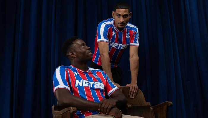 Camisa titular Crystal Palace Macron 2025/26 listrada em azul e vermelho com detalhes em branco
