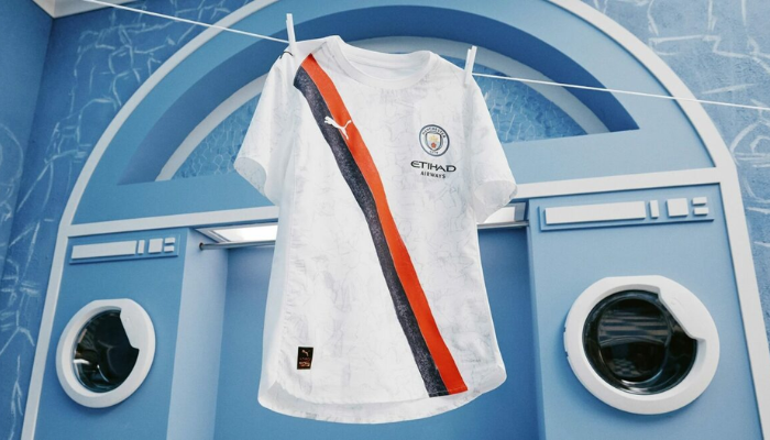 Camisa titular Manchester City 2025/26 Puma x KidSuper branca com faixa diagonal rubro-negra e detalhes artísticos