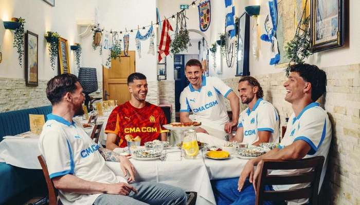 Camisa titular Olympique Marseille Puma 2025/26 branca com detalhes em azul celeste e logos históricos em marca d’água.