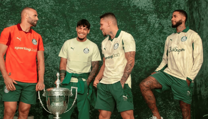 Camisa titular Palmeiras 2025 dourada com gola polo verde, grafismo barroco de folhas, escudo do clube à esquerda, logos da PUMA e KidSuper em verde, homenagem ao Mundial de 1951