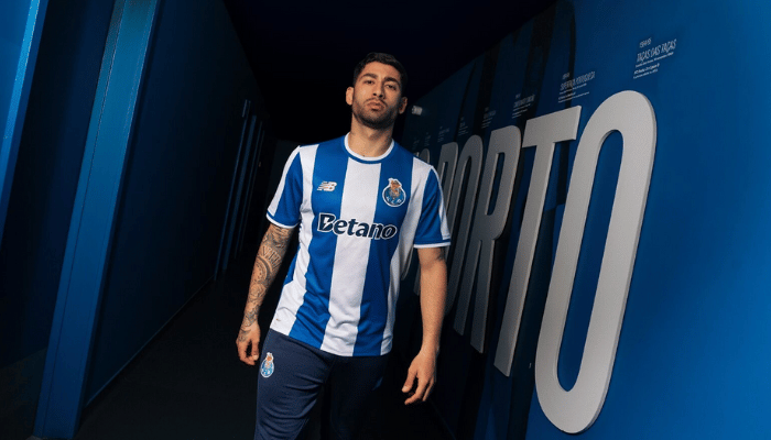 Camisa titular Porto FC 2025 New Balance branca, azul e dourada com listras verticais, gola redonda bicolor, escudo no peito, logo NB dourado e detalhe “Aniversár10” no colarinho.