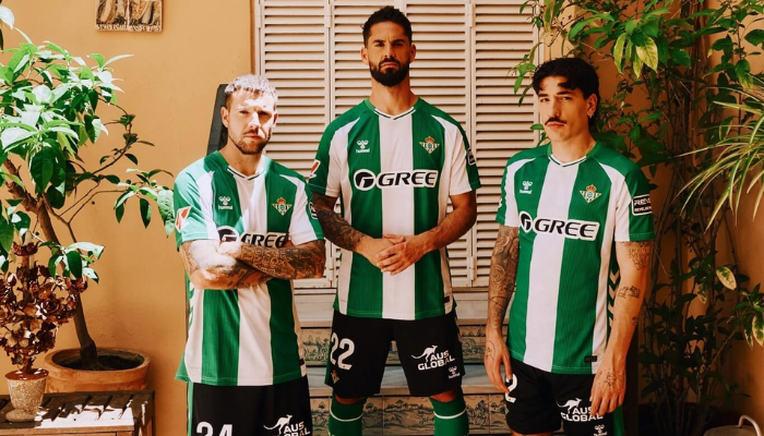Camisa home Real Bétis 2025/26 branca e verde com listras largas, gola V e frase “Verde, verde como o time da minha cidade”, logo Hummel e escudo do Bétis