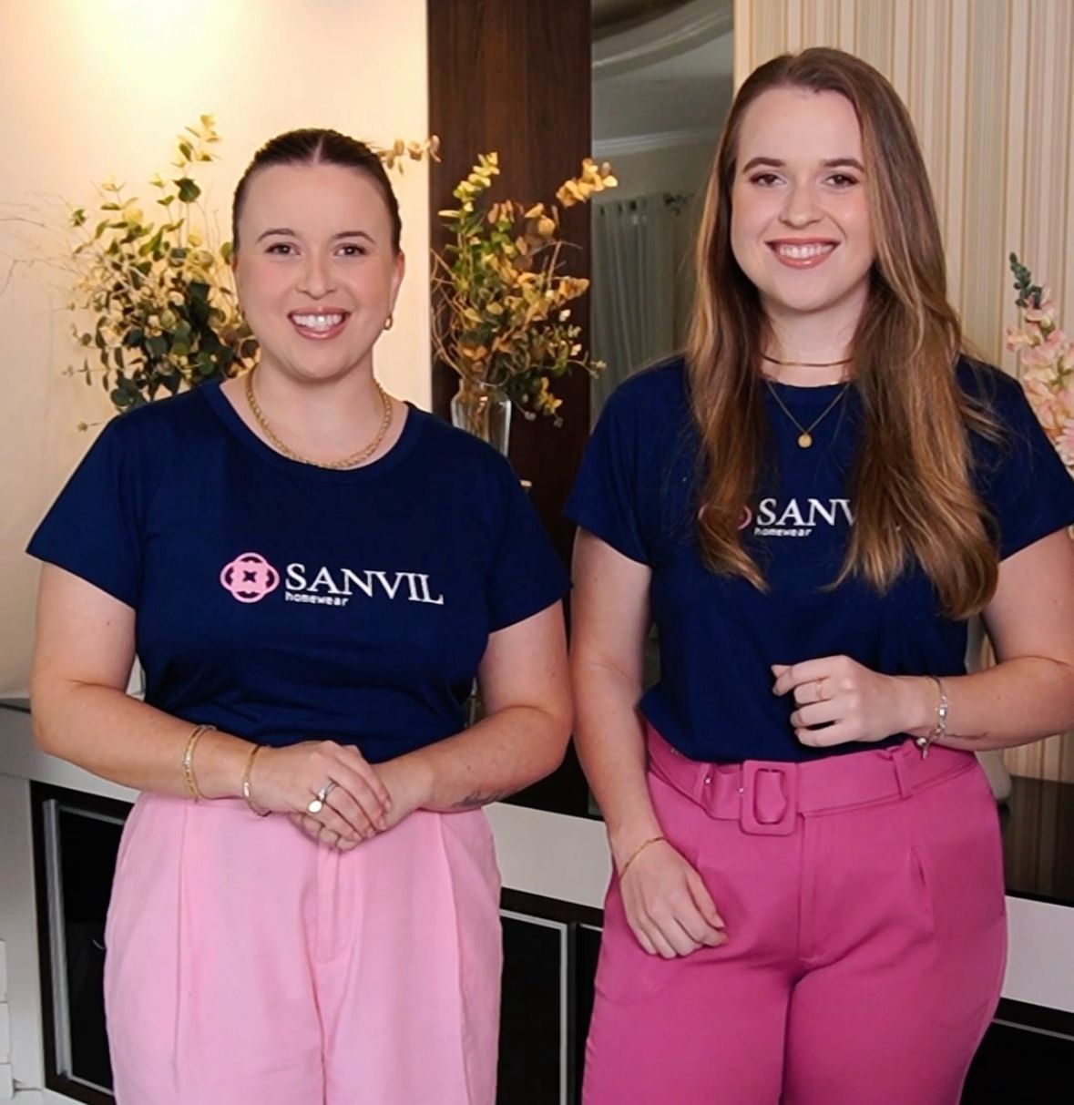 Duas mulheres sorridentes vestem camisetas azul marinho com a logomarca Sanvil estampada e calça rosa