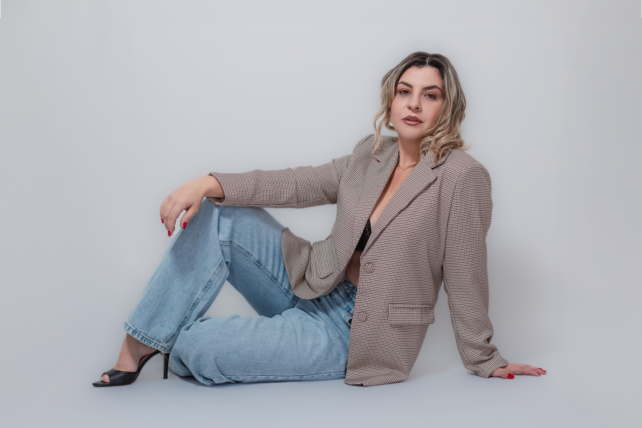 Lu (mulher, vestida de um blazer e calça jeans), sentando no chão em um fundo branco