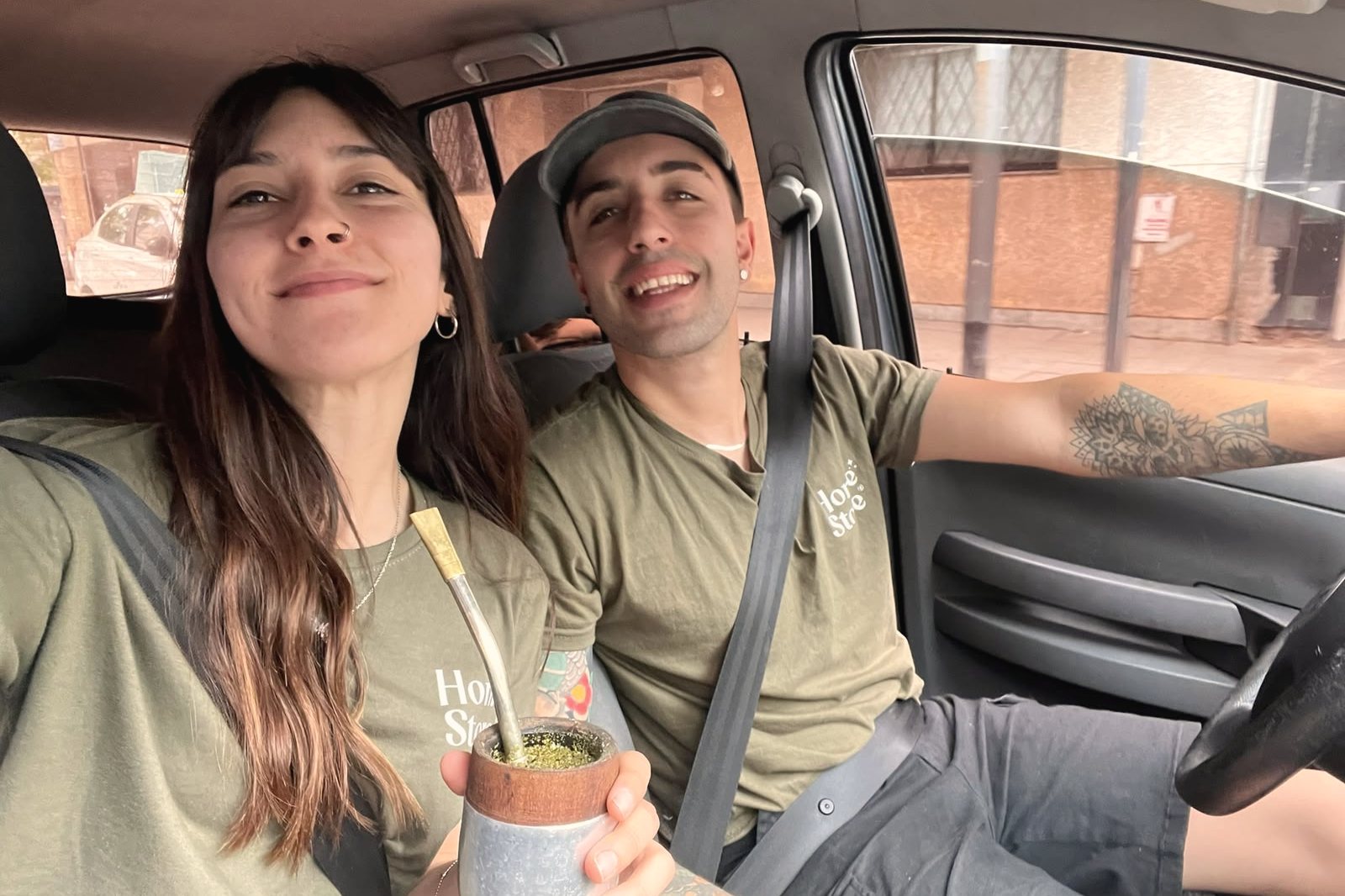 Belén y Hernán con remeras de Home Store tomando mate en el auto