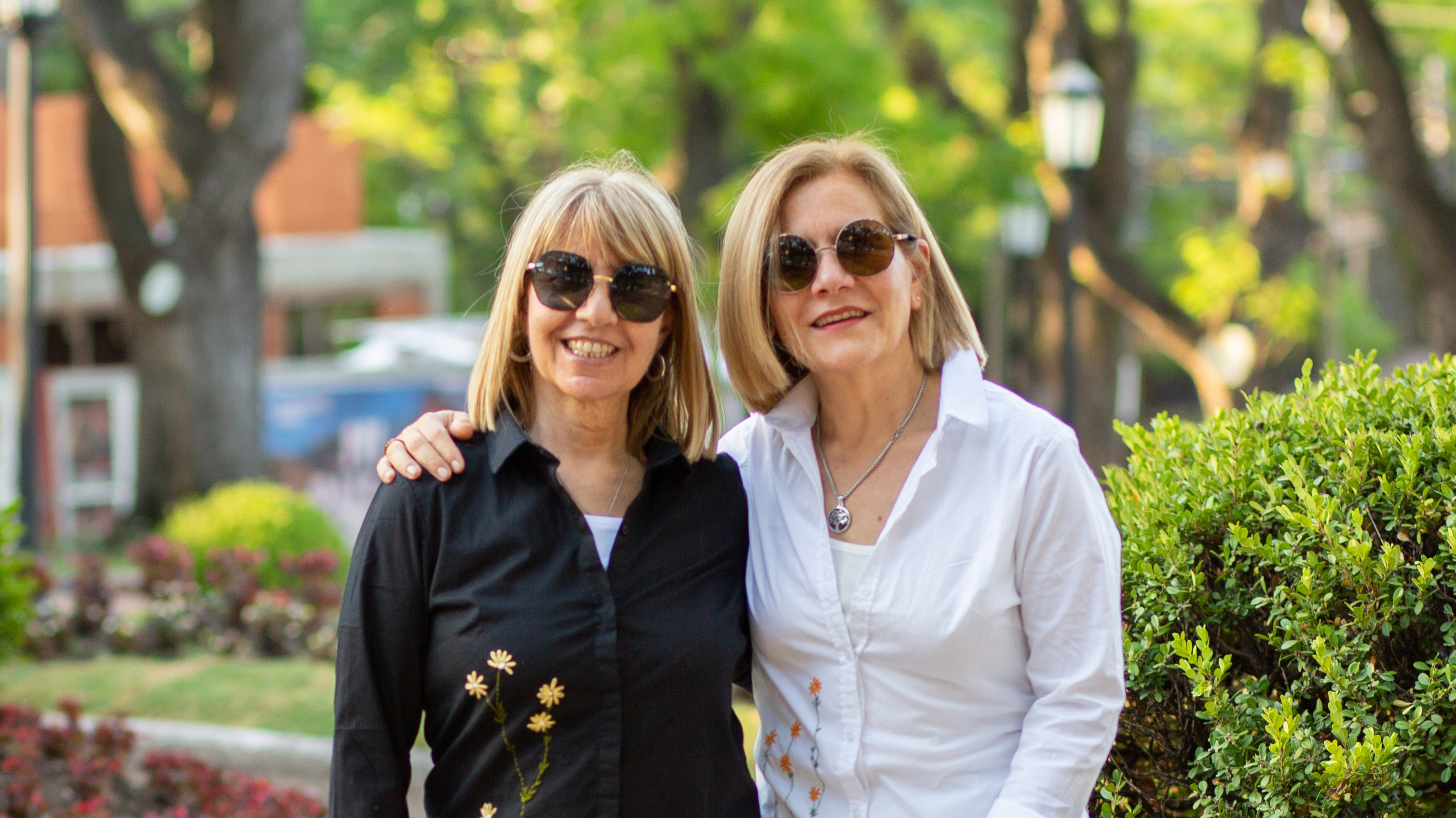 Fotografía de Maru y Andrea abrazadas mirando a la cámara con un fondo de árboles y arbustos