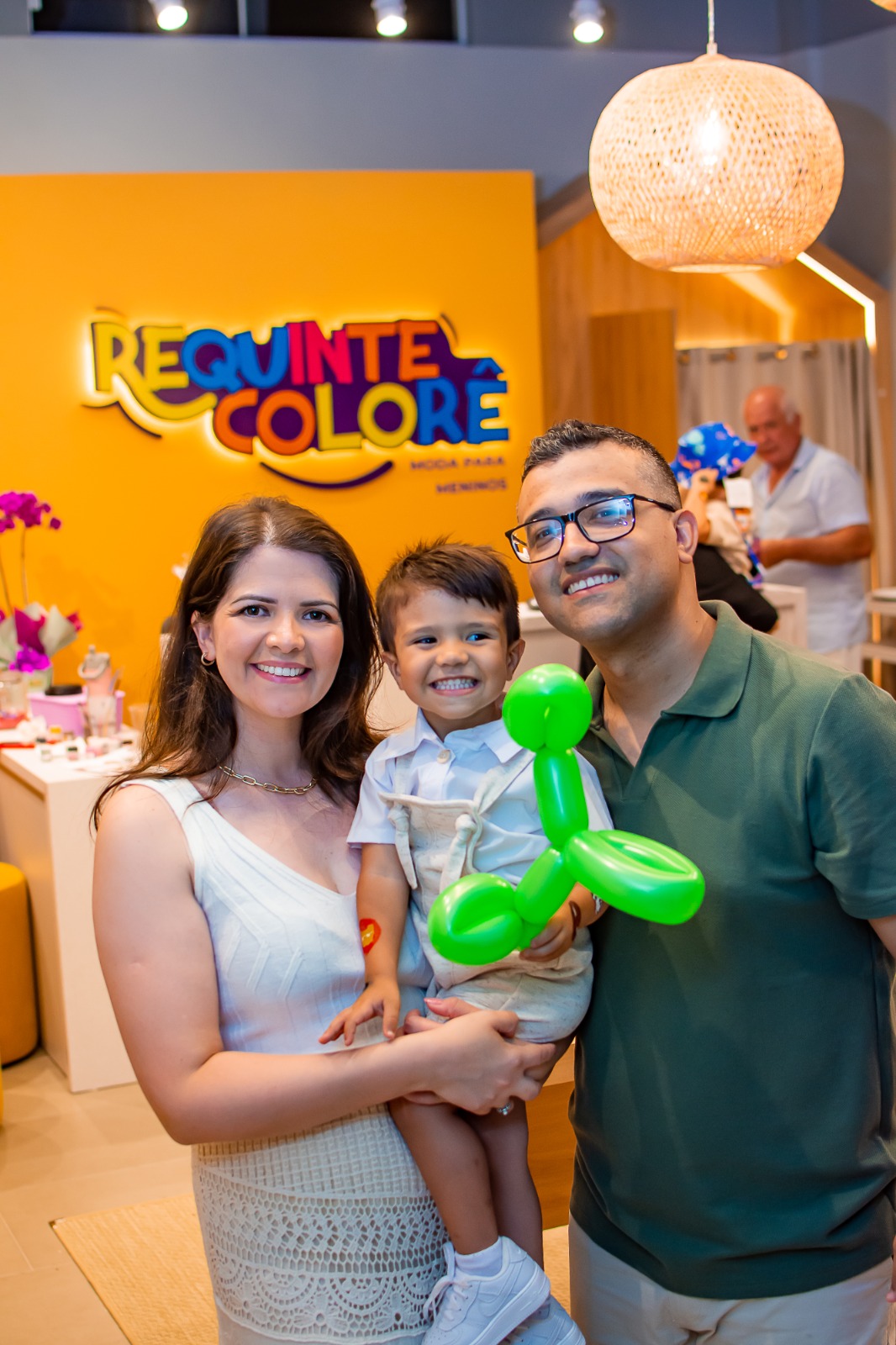 Dois adultos e uma criança em frente à marca Requinte Colorê, no interior da loja.