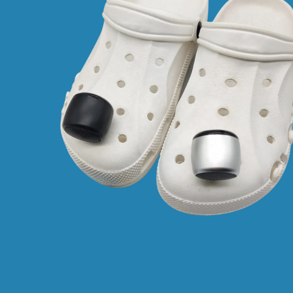 dos mini parlantes bluetooth para crocs sobre un par de crocs blancas