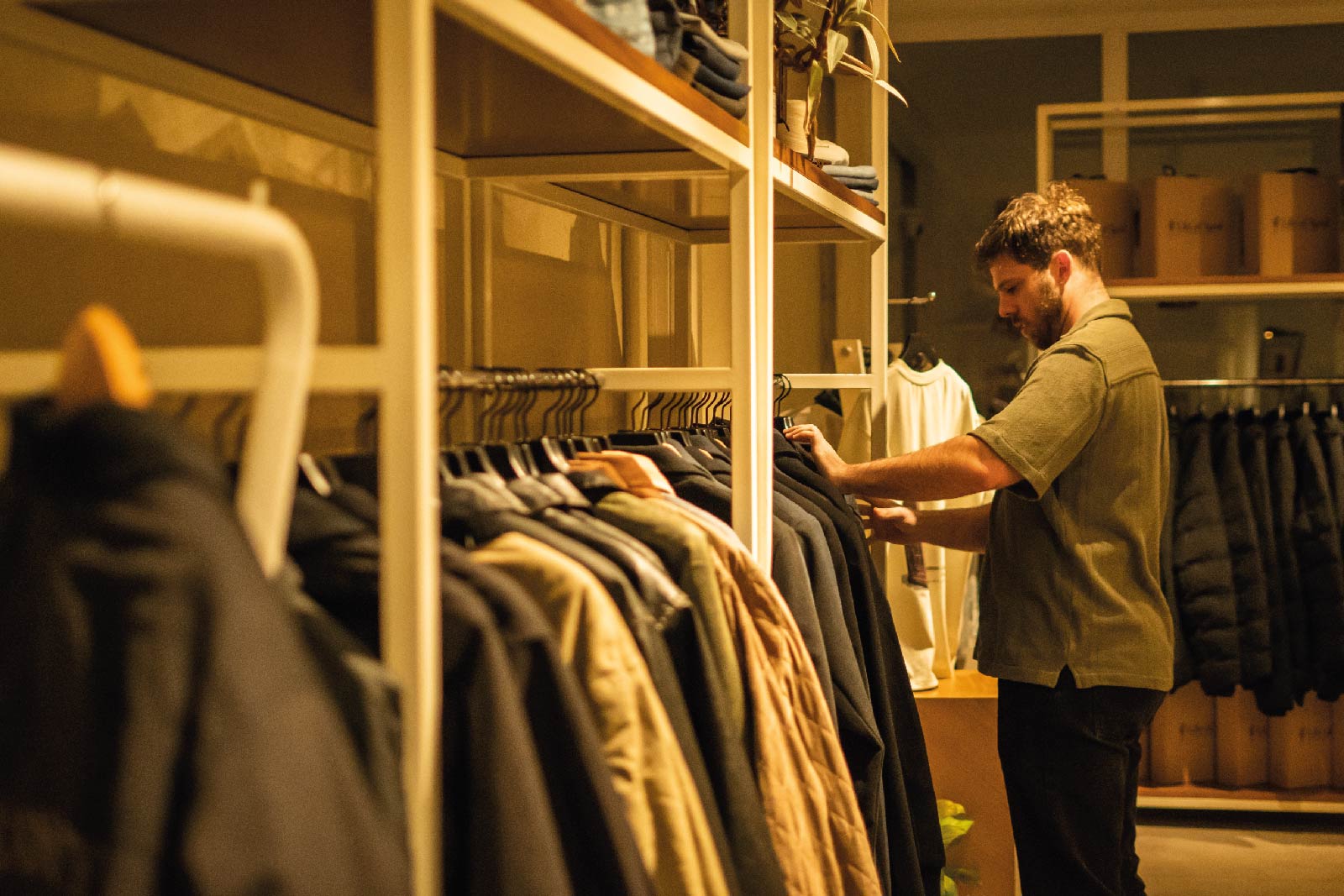 Showroom de House of Tyrol: un hombre revisa camperas y abrigos colgados en los percheros, con luz cálida.
