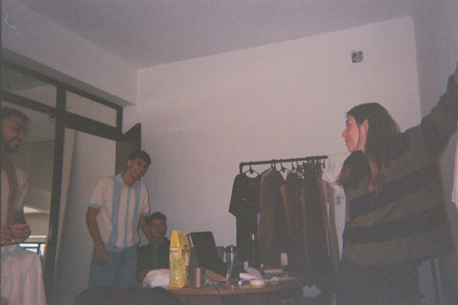 Foto analógica en la oficina de House of Tyrol: personas charlando junto a un perchero con ropa y una mesa de trabajo.