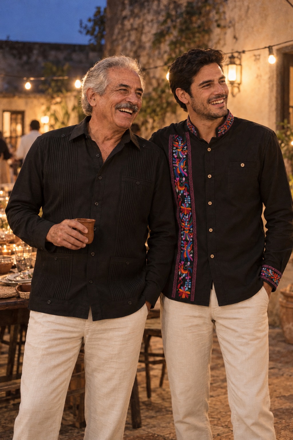 Dos hombres de distinta edad con una Guayabera Presidencial Negra y una Camisa Alebrije Negra en una velada nocturna en un patio