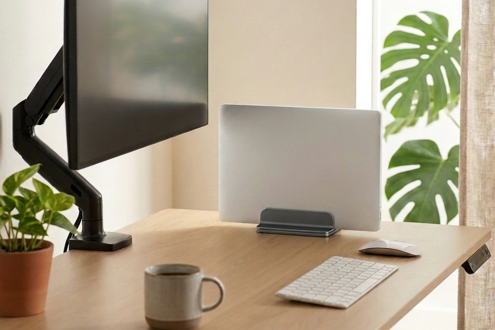Setup con standing desk, monitor elevado y notebook cerrada en el soporte vertical de aluminio gris oscuro
