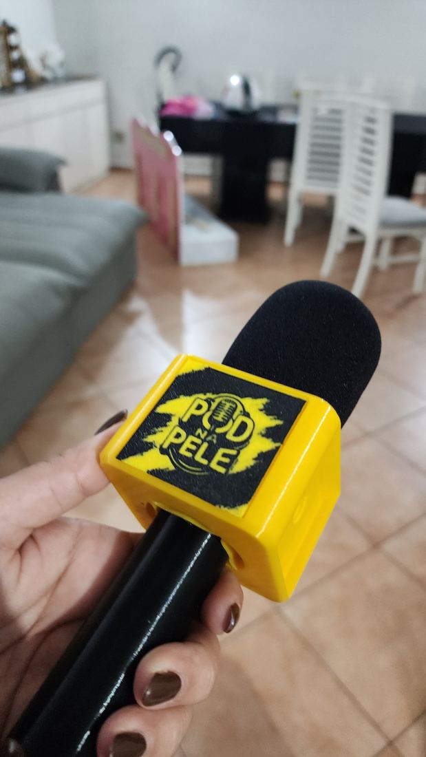Canopla amarela com a logo do podcast Pod na Pele encaixada em um microfone de mão