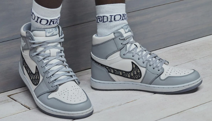 Tênis Dior x Air Jordan 1 High branco e cinza em couro italiano com Swoosh Dior Oblique e sola translúcida.