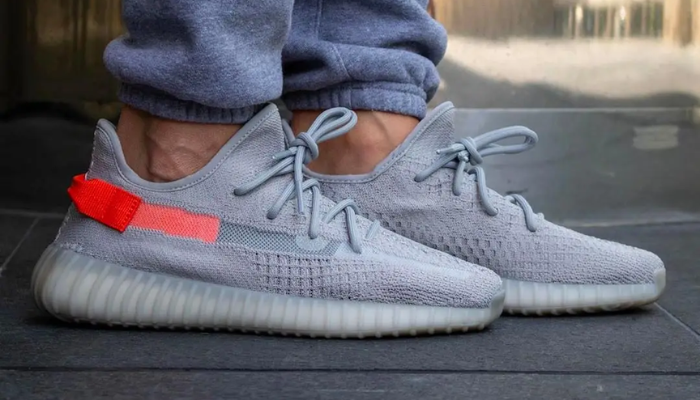 Tênis Yeezy Boost 350 V2 Tail Light em Primeknit cinza com detalhe laranja no calcanhar.