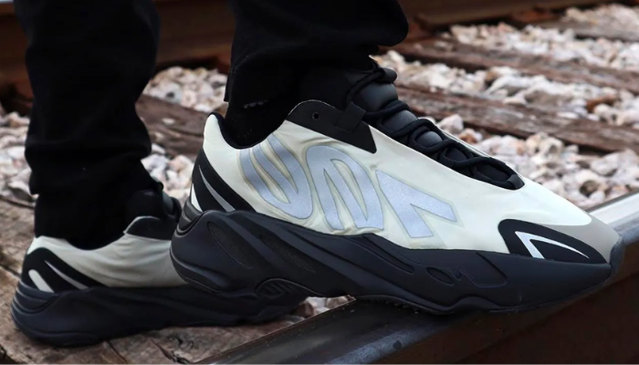 Tênis Yeezy Boost 700 MNVN Bone creme com sobreposições pretas e detalhes refletivos “700” nas laterais.