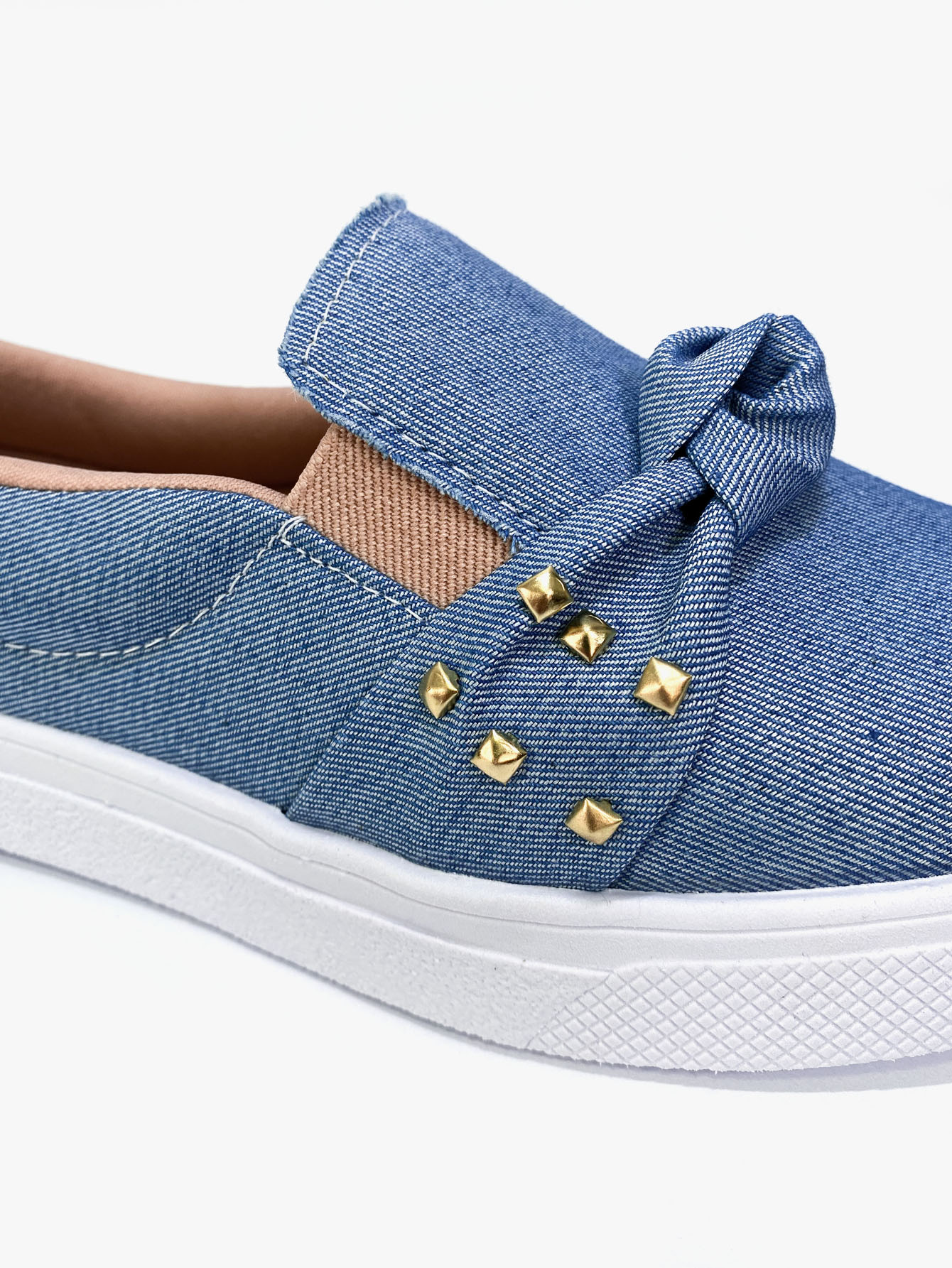 Detalhe do slip on jeans com laço e tachinhas douradas