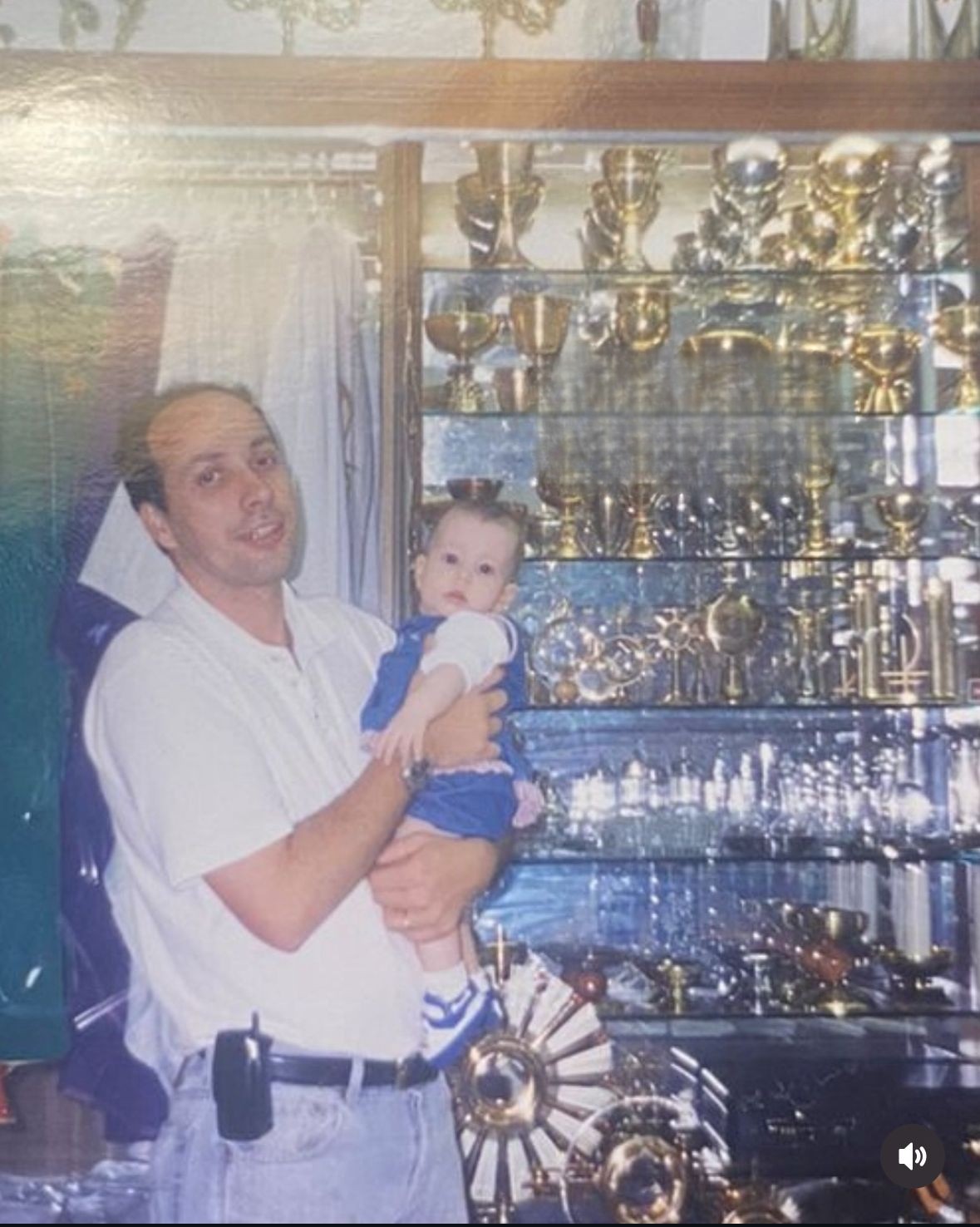 André Bernardi com a filha bebê em colo, dentro da Livraria Santa Fé em 2002, com a vitrine de cálices ao fundo
