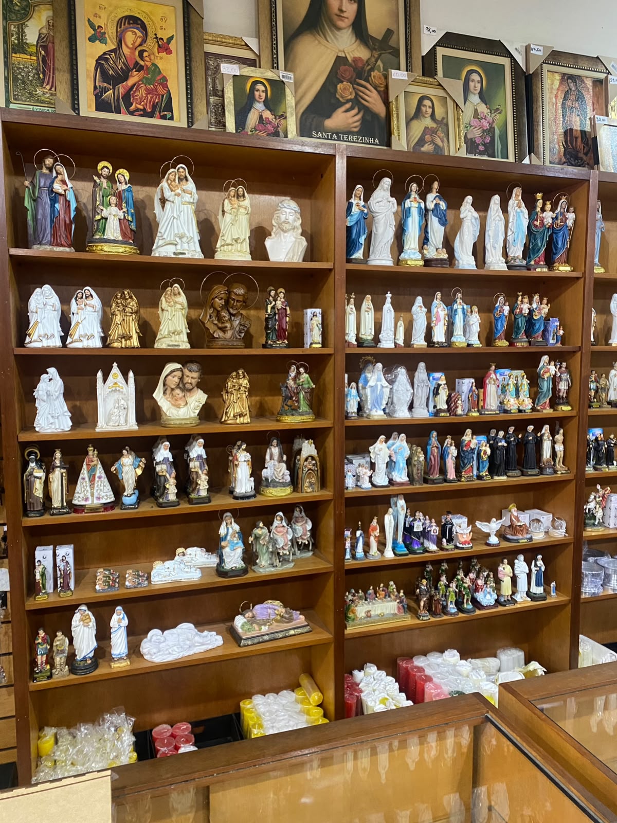 Vista interna da Livraria Santa Fé: prateleiras de madeira clara com imagens católicas em fileiras